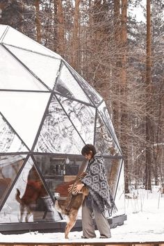 a man standing in front of a large glass structure with animals inside it on top of snow covered ground