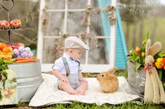 a baby is sitting on a blanket next to some flowers and carrots with a bunny