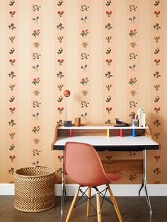 a desk and chair in front of a wallpapered room with flowers on it