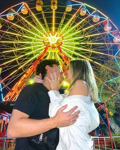 a man and woman are kissing in front of a ferris wheel at an amusement park