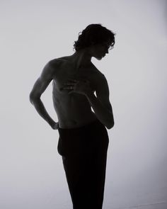 a shirtless man standing in front of a white wall with his hands on his hips