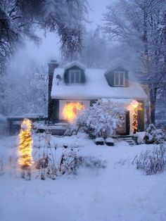 a house is covered in snow with christmas lights on the windows and trees around it