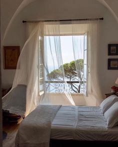 a bed sitting under a window next to a white curtained wall with a balcony