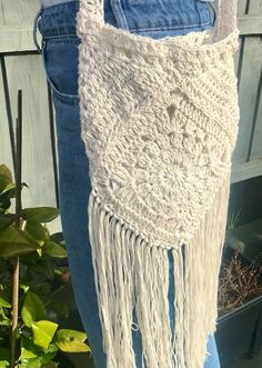 a white crocheted bag with fringes hanging from it's side, in front of a plant