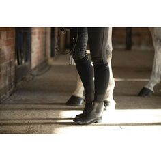 a person standing next to a horse in a stable with their legs on the ground