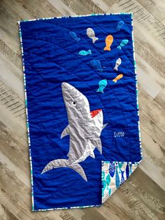 a blue quilt with a shark and fish design on the front is laying on a wooden floor