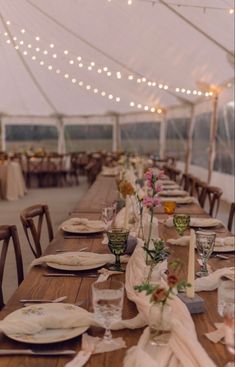 a long table set with plates and napkins under a tented area for dinner