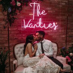 a man and woman sitting on a chair in front of a neon sign that reads the valentine's