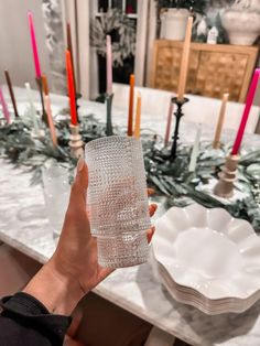 a person holding a glass in front of a table with candles and plates on it