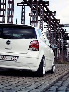 the back end of a white car parked on a cobblestone road with scaffolding in the background