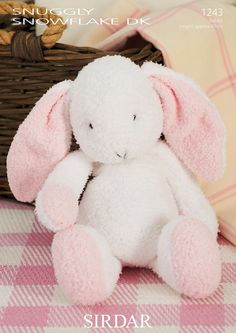 a pink and white stuffed animal sitting on top of a blanket next to a basket