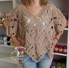 a woman standing in front of a shelf with crocheted sweaters on it