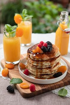 a stack of pancakes sitting on top of a wooden cutting board next to orange juice