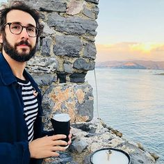 a man standing next to a stone wall holding a cup