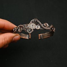 a hand holding a piece of metal that is shaped like a bracelet with spirals on it