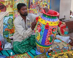 a man sitting on the ground working on a large vase with colorful decorations around it