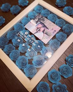 blue paper flowers are arranged in a square frame on a wooden table with a photo