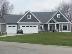 a car is parked in front of a large gray house with two garages on each side