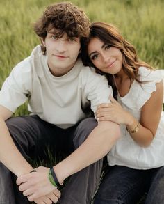 a young man and woman are sitting in the grass, posing for a photo with their arms around each other