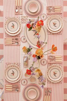 the table is set with pink and white plates, silverware, and floral centerpieces