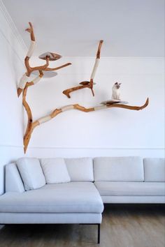 a white couch sitting in front of a wall mounted tree branch with a cat on it