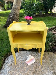 a yellow table with a flower pot on top and a pink flower in the middle