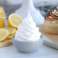 two cupcakes with white frosting and lemon slices next to them on a cutting board