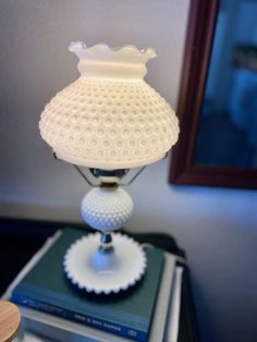 a white lamp sitting on top of a stack of books next to a mirror and bookcase