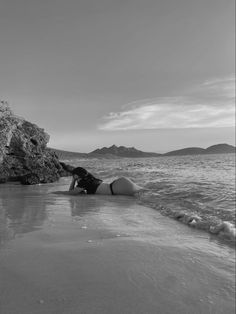 a woman laying on top of a sandy beach next to the ocean