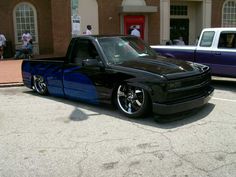 a black truck with blue stripes parked in front of a building next to other cars