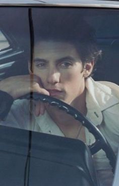 a man sitting in the driver's seat of a car with his hand on the steering wheel