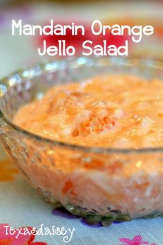 an orange jello salad in a glass bowl on a colorful tablecloth with the words mandarin orange jello salad above it