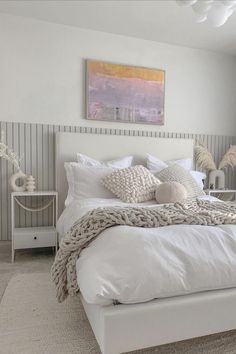 a white bed sitting in a bedroom next to a painting on the side of a wall