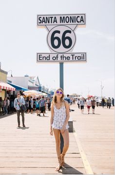 a woman standing under a sign that says santa monica 66 end of the trail