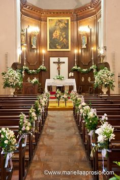 the interior of a church with pews and flowers on the aisle, decorated with greenery