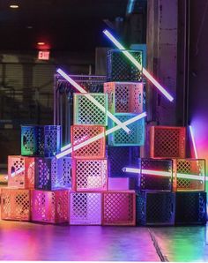 many different colored boxes stacked on top of each other in front of a neon light