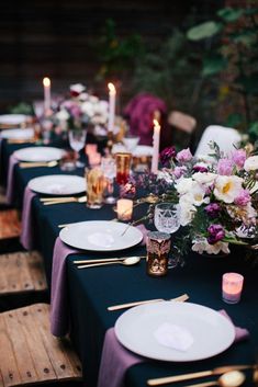 the table is set with purple and white flowers, candles, and place settings for dinner