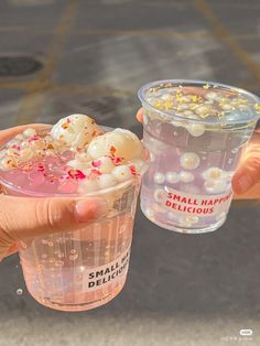 two people holding up plastic cups filled with small bubbles and sprinkles on them