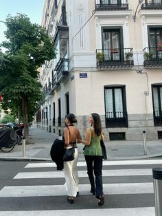 two women walking across a cross walk in front of tall buildings with balconies