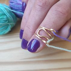 a woman's hand with purple and gold nail polish on it, next to yarn