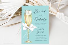 a blue and white wedding card with a champagne glass on it next to palm leaves