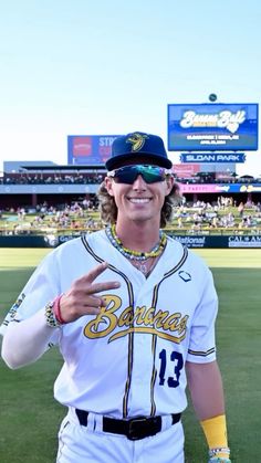 a baseball player is standing in the outfield with his hand up and wearing sunglasses