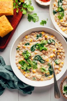 Bowls of creamy vegan white bean chili next to cayenne, cilantro, and cornbread