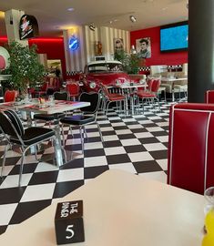 a restaurant with black and white checkered flooring, red booths, and tables