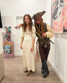 a man and woman dressed up as pirates in an art gallery with paintings on the wall