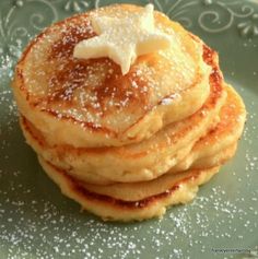 a stack of pancakes topped with butter and powdered sugar on a green platter