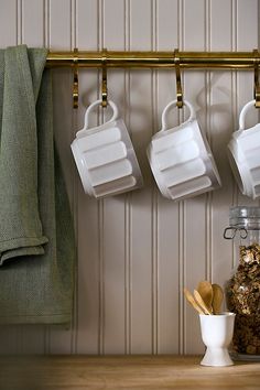 three mugs hanging on the wall with spoons and spices in front of them