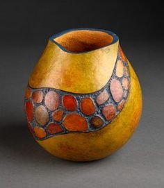 a yellow vase sitting on top of a gray table next to a black wall with circles painted on it