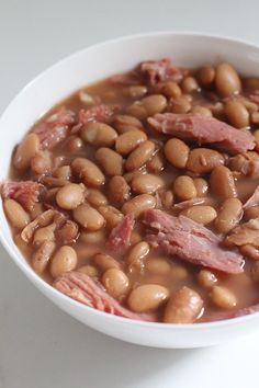 a white bowl filled with ham and pinto bean soup on top of a white table