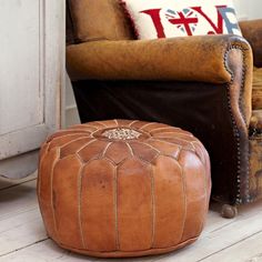 a brown leather ottoman sitting on top of a wooden floor next to an old chair